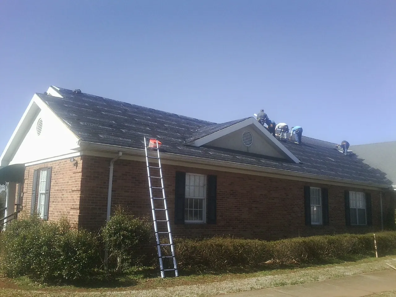 Crew tearing shingles off a brick ranch roof with a ladder set — Emergency Roof Repair work by our crew in Eugene