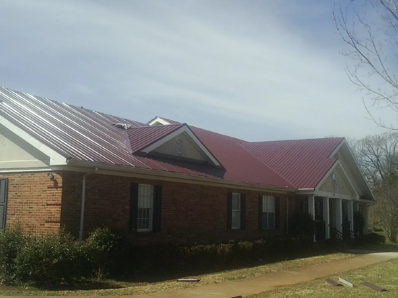Red metal roof with gabled entries on a long brick building, from a Hail Damage Roof Repair job in Eugene