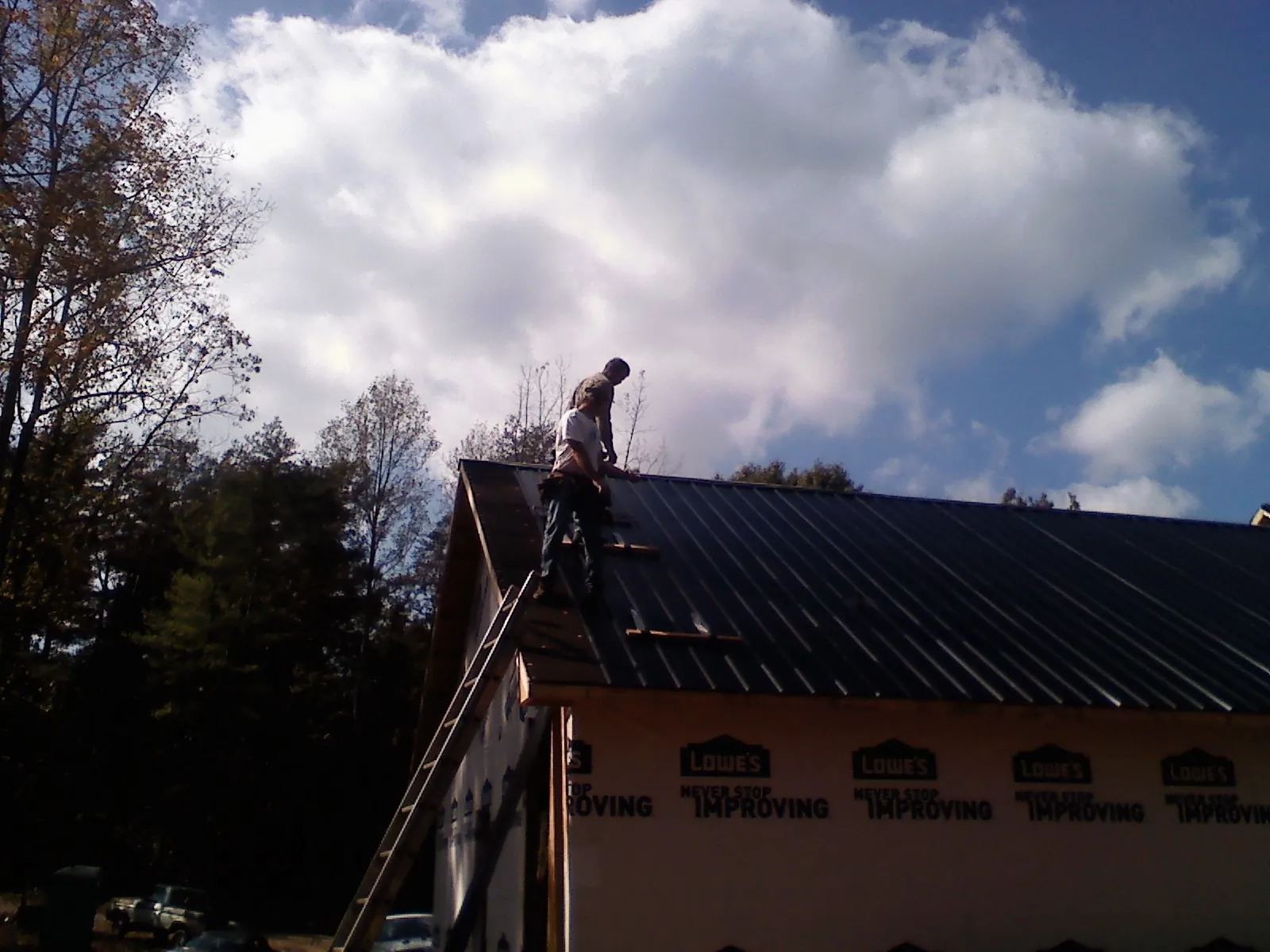 Roofer fastening dark metal panels high against a cloudy sky, from a Roof Inspection job in Eugene